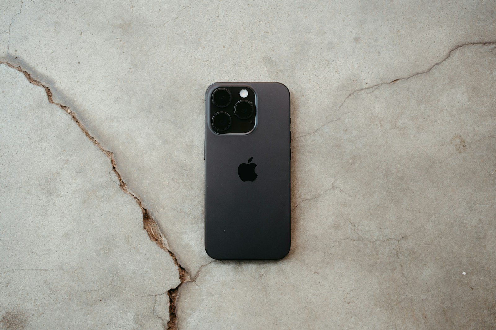 An apple iPhone is on a cracked surface.