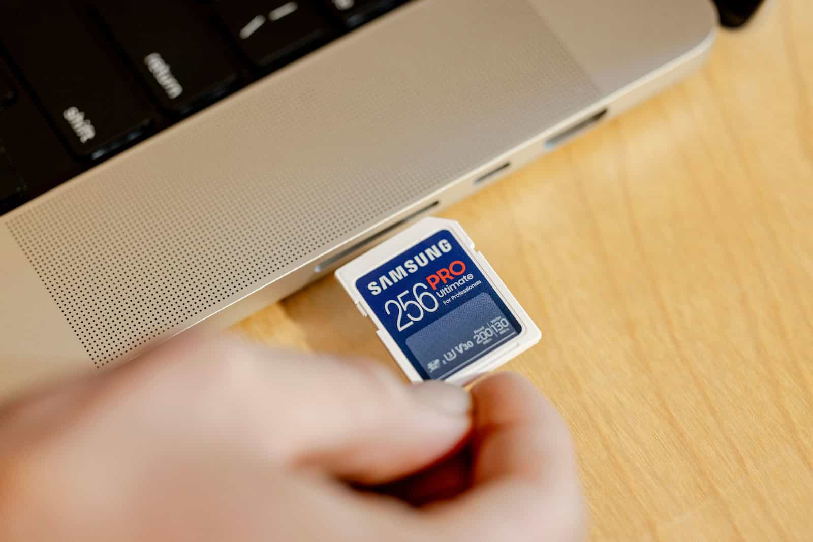 A person holding a micro sd card in front of a laptop