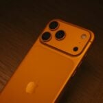 Back of an orange smartphone with three cameras.