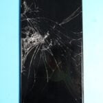 Broken smartphone screen on a blue surface.