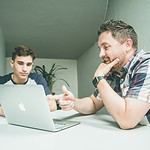 man wearing white and black plaid button-up sports shirt pointing the silver MacBook